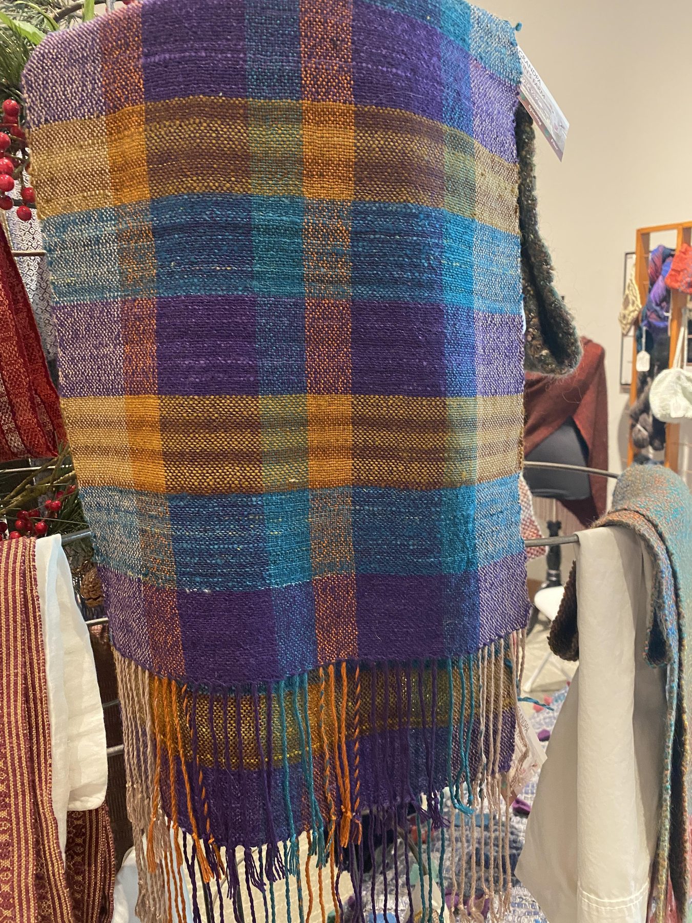 Purple, teal, and gold plaid handwoven scarf on display at a Montana market booth